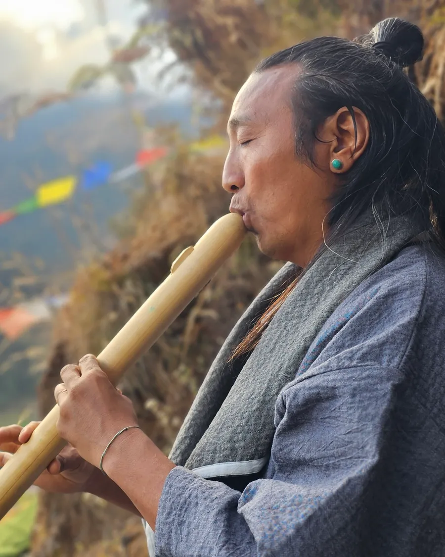 Pasang Lama jouant de la flûte de bambou, drapeaux de prières au vent dans la montagne